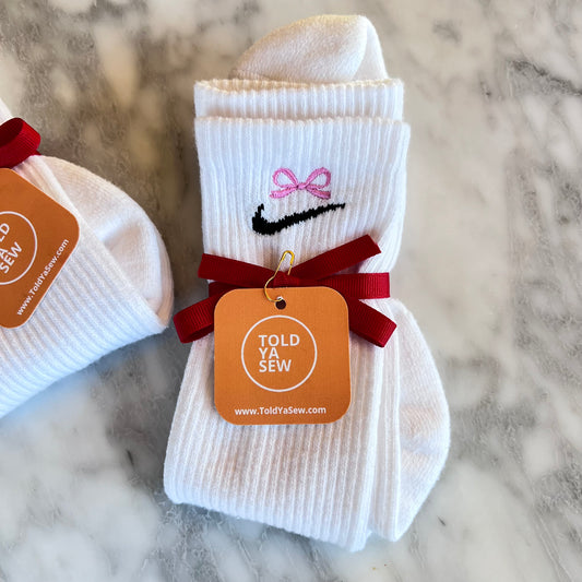 A pair of Nike white crew socks with  bow embroidery.